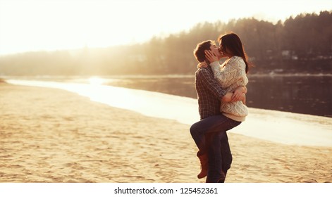 Jovem belo casal apaixonado ficar e beijar na praia ao pôr do sol. Cores suaves e ensolaradas.