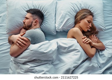 Young Beautiful Couple Lying In Bed Turned Back To Back, Arms Crossed In Anger And Resentment. Relationship Problems.Top View.