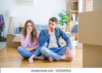Young beautiful couple moving to a new house sitting on the floor looking stressed and nervous with hands on mouth biting nails. Anxiety problem.
