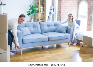 Young Beautiful Couple Moving Sofa At New Home Around Cardboard Boxes