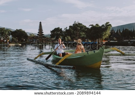Young beautiful couple paddling on a wooden boat at Pura Ulun Danu Bratan, Bali - Tourists exploring Bali