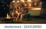 Young Beautiful Couple Relaxing at a Caravan Camping Area in the Evening, Keeping Warm with Campfire, Plaid Blanket and Warm Tea. Looking at the Stars and Wandering About a Successful Future Together.