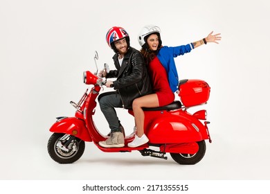 Young Beautiful Couple Riding A Vintage Red Electric Motorbike Scooter Happy Having Fun Together, Stylish Hipster Man And Woman Isolated On White Studio Background Wearing Safety Helmets On Speed