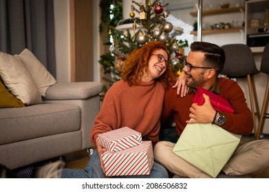 Young beautiful couple sitting on the apod next to the Christmas tree and enjoying the holidays