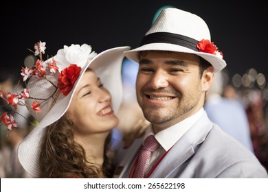 Young Beautiful Couple Smiling And Laughing While Wearing Flower Hats At The Dubai World Cup Horse Race