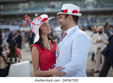 Young Beautiful Couple Smiling And Laughing While Wearing Flower Hats At The Dubai World Cup Horse Race