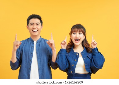 Young beautiful couple standing over isolated yellow background amazed and surprised looking up and pointing with fingers and raised arms.