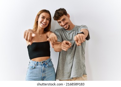 Young beautiful couple standing together over isolated background pointing to you and the camera with fingers, smiling positive and cheerful 