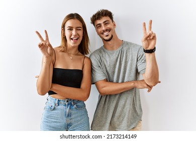 Young beautiful couple standing together over isolated background smiling with happy face winking at the camera doing victory sign with fingers. number two. 
