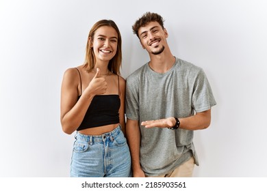 Young beautiful couple standing together over isolated background showing palm hand and doing ok gesture with thumbs up, smiling happy and cheerful 