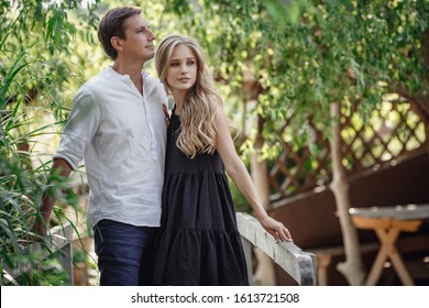 Young beautiful couple in the summer garden enjoys tranquility and relaxation. Happy couple on vacation. Lovers are laughing. Happy guy and girl. Lovers enjoy each other in the evening park.
