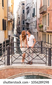 young beautiful couple tourists red-haired girl in white dress and man in white clothes stand on a bridge near a canal in the beautiful city of Venice in Italy