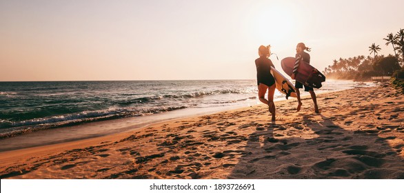 Young beautiful couple walking along the sandy beach near the ocean at sunset with surfboards, outdoor activities - Powered by Shutterstock