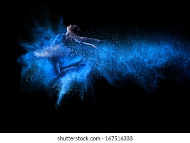 Young beautiful dancer jumping into blue powder cloud 