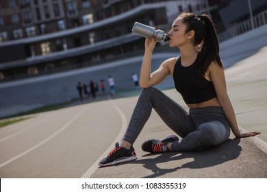 A Young Beautiful Dark-haired Athletic Girl Is Hanging Out In Sports, Warming Up And Performing Sports Exercises For Her Health And A Strong Healthy Body On A Treadmill On The City Street Cycle Track