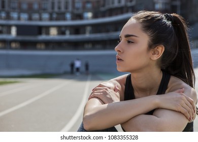 A Young Beautiful Dark-haired Athletic Girl Is Hanging Out In Sports, Warming Up And Performing Sports Exercises For Her Health And A Strong Healthy Body On A Treadmill On The City Street Cycle Track