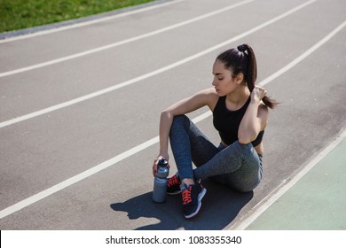 A Young Beautiful Dark-haired Athletic Girl Is Hanging Out In Sports, Warming Up And Performing Sports Exercises For Her Health And A Strong Healthy Body On A Treadmill On The City Street Cycle Track