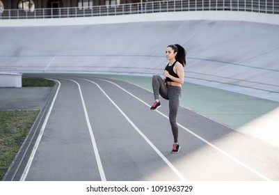 A Young Beautiful Dark-haired Athletic Girl Is Hanging Out In Sports, Warming Up And Performing Sports Exercises For Her Health And A Strong Healthy Body On A Treadmill On The City Street Cycle Track