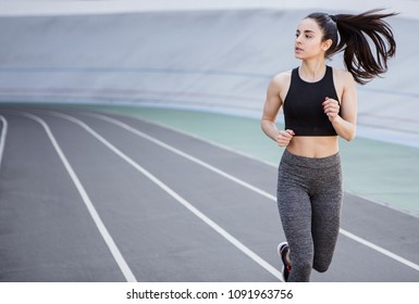 A Young Beautiful Dark-haired Athletic Girl Is Hanging Out In Sports, Warming Up And Performing Sports Exercises For Her Health And A Strong Healthy Body On A Treadmill On The City Street Cycle Track