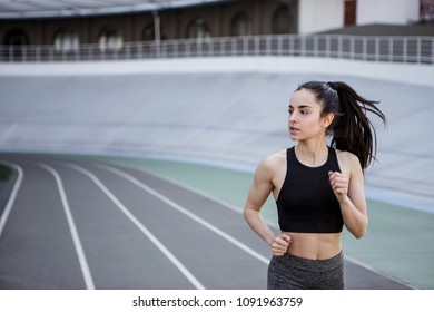 A Young Beautiful Dark-haired Athletic Girl Is Hanging Out In Sports, Warming Up And Performing Sports Exercises For Her Health And A Strong Healthy Body On A Treadmill On The City Street Cycle Track