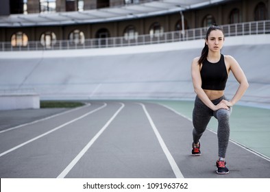 A Young Beautiful Dark-haired Athletic Girl Is Hanging Out In Sports, Warming Up And Performing Sports Exercises For Her Health And A Strong Healthy Body On A Treadmill On The City Street Cycle Track