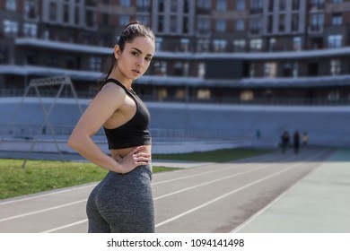 A Young Beautiful Dark-haired Athletic Girl Is Hanging Out In Sports, Warming Up And Performing Sports Exercises For Her Health And A Strong Healthy Body On A Treadmill On The City Street Cycle Track