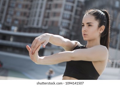 A Young Beautiful Dark-haired Athletic Girl Is Hanging Out In Sports, Warming Up And Performing Sports Exercises For Her Health And A Strong Healthy Body On A Treadmill On The City Street Cycle Track