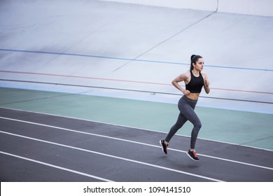 A Young Beautiful Dark-haired Athletic Girl Is Hanging Out In Sports, Warming Up And Performing Sports Exercises For Her Health And A Strong Healthy Body On A Treadmill On The City Street Cycle Track