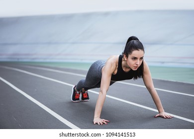 A Young Beautiful Dark-haired Athletic Girl Is Hanging Out In Sports, Warming Up And Performing Sports Exercises For Her Health And A Strong Healthy Body On A Treadmill On The City Street Cycle Track