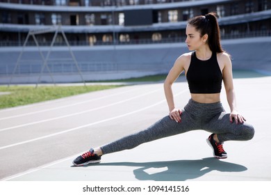 A Young Beautiful Dark-haired Athletic Girl Is Hanging Out In Sports, Warming Up And Performing Sports Exercises For Her Health And A Strong Healthy Body On A Treadmill On The City Street Cycle Track