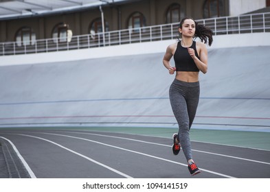 A Young Beautiful Dark-haired Athletic Girl Is Hanging Out In Sports, Warming Up And Performing Sports Exercises For Her Health And A Strong Healthy Body On A Treadmill On The City Street Cycle Track