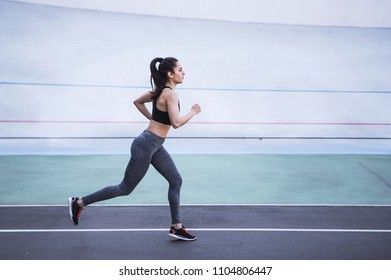 A Young Beautiful Dark-haired Athletic Girl Is Hanging Out In Sports, Warming Up And Performing Sports Exercises For Her Health And A Strong Healthy Body On A Treadmill On The City Street Cycle Track