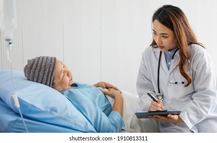 Young and beautiful doctor asking and note for diagnosis with Older Asian woman patient covered the head with clothes effect from chemo treatment in cancer cure process.