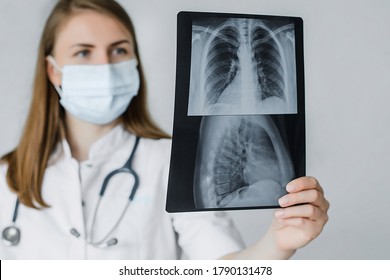 Young Beautiful Doctor Radiologist Look Learn Waych Human Skeleton Of Lungs. A Woman In A White Coat With A Mask And Stethoscope On Her Neck Is Studying Fluorography.