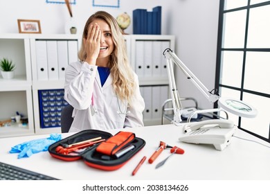 Young Beautiful Doctor Woman With Reflex Hammer And Medical Instruments Covering One Eye With Hand, Confident Smile On Face And Surprise Emotion. 