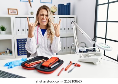 Young Beautiful Doctor Woman With Reflex Hammer And Medical Instruments Shouting With Crazy Expression Doing Rock Symbol With Hands Up. Music Star. Heavy Concept. 