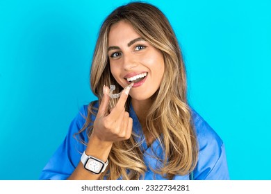 young beautiful doctor woman standing over blue studio background holding an invisible aligner ready to use it. Dental healthcare and confidence concept.