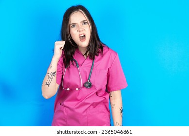 young beautiful doctor woman standing over blue background angry and mad raising fist frustrated and furious while shouting with anger. Rage and aggressive concept. - Shutterstock ID 2365046861