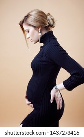 Young beautiful elegant and stylish pregnant woman in black clothes on a beige neutral background.