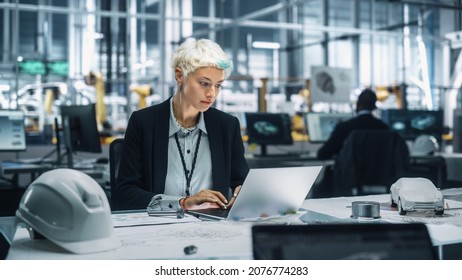 Young Beautiful Engineer Working and Managing Projects on Laptop Computer in an Office at Car Assembly Plant. Industrial Specialist Working on Vehicle Parts in Technological Development Facility. - Powered by Shutterstock