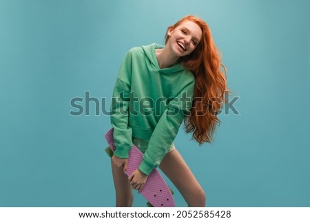 Young beautiful european red-haired girl in casual body shirt with happy and cool smile on face. Her hair falls to side. Skateboard concept.