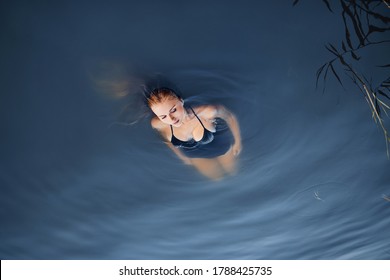 Young Beautiful European Woman With Wet White Blond Hair In A Black Swimsuit Swiming In The Water In A Lake. Relaxing Beauty Fashion Concept