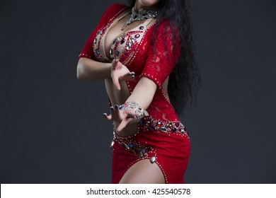 Young beautiful exotic eastern women performs belly dance in ethnic red dress on gray background. Studio shot