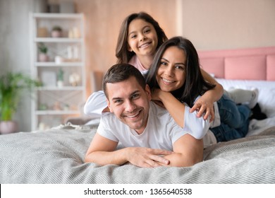 Young beautiful family hug each other while lying in bed with look in camera - Powered by Shutterstock