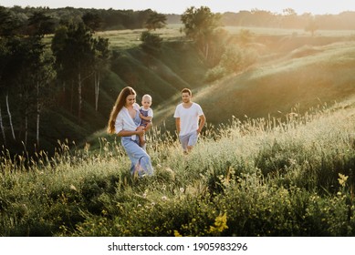 Young Beautiful Family With A Little Daughter Hug, Kiss And Walk In Nature At Sunset. Photo Of A Family With A Small Child In Nature.