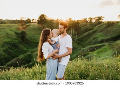 Young Beautiful Family With A Little Daughter Hug, Kiss And Walk In Nature At Sunset. Photo Of A Family With A Small Child In Nature.