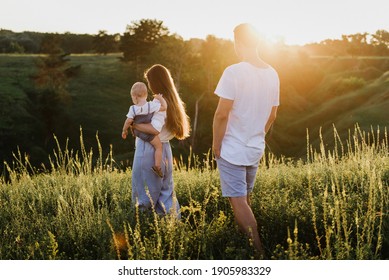 Young Beautiful Family With A Little Daughter Hug, Kiss And Walk In Nature At Sunset. Photo Of A Family With A Small Child In Nature.