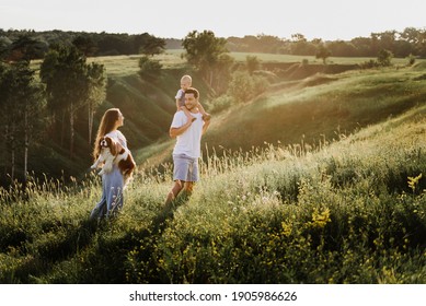 Young Beautiful Family With A Little Daughter Hug, Kiss And Walk In Nature. Photo Of A Family With A Small Child In Nature.