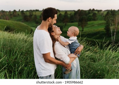 Young Beautiful Family With A Little Daughter Hug, Kiss And Walk In Nature. Photo Of A Family With A Small Child In Nature.