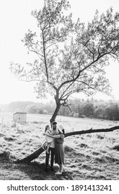 Young beautiful family near the tree. There is a cabin on the background. Black and white photo.